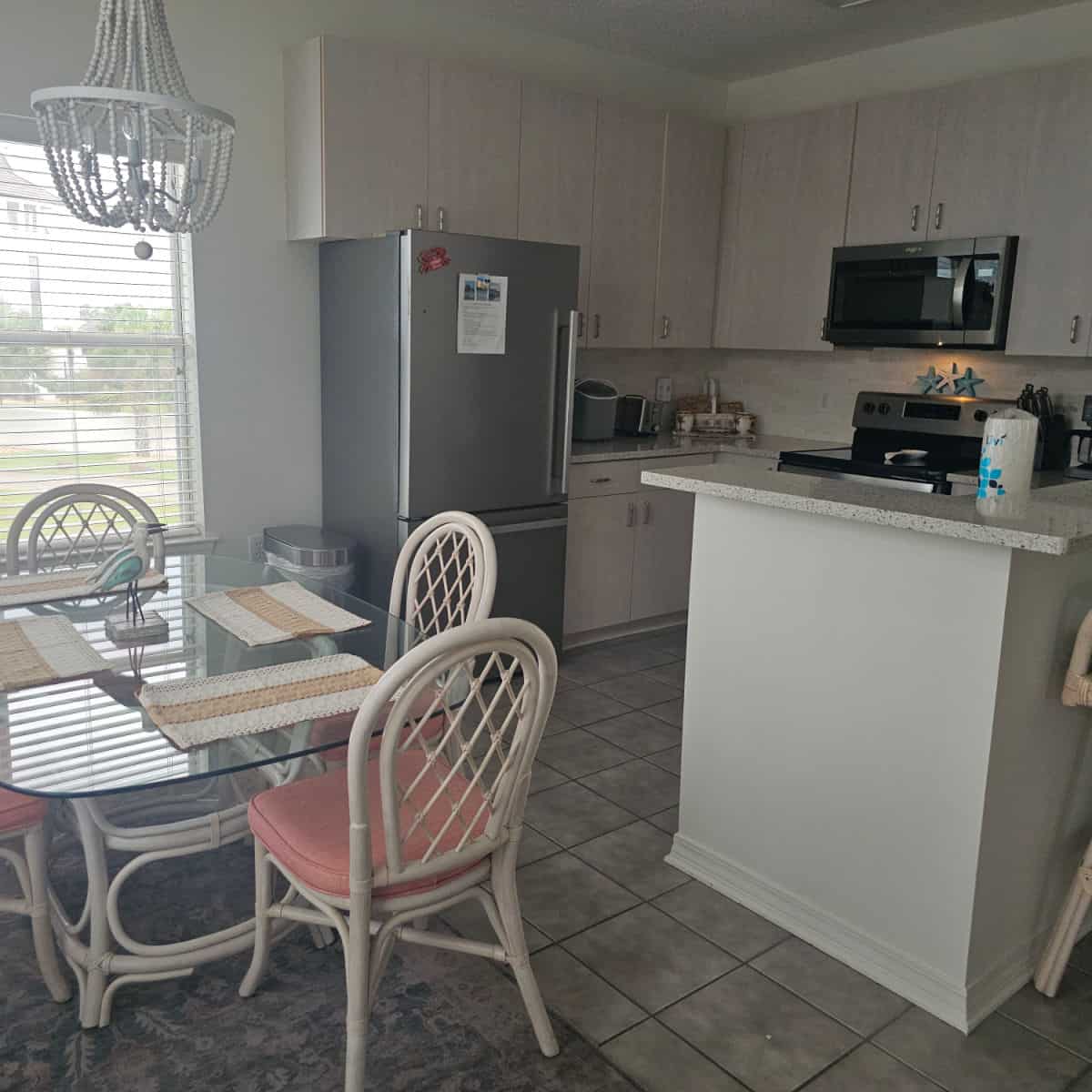 kitchen area with grey cabinets and stainless steel appliances, glass dining room table with white chairs.