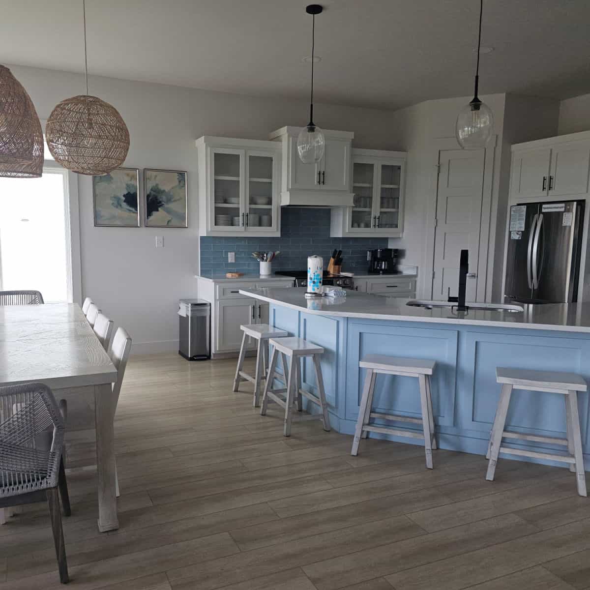 kitchen with blue cabinets under the white island counter and white stools, white cabinets with stainless steel appliances and pendant lamps