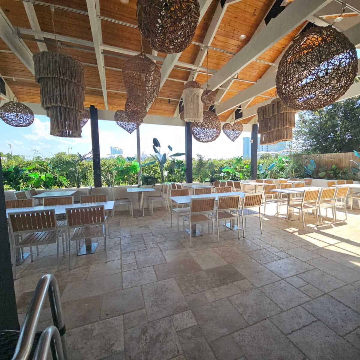 outdoor seating with tables and chairs, tropical plants around the edges, lots of lights hanging from the ceiling.