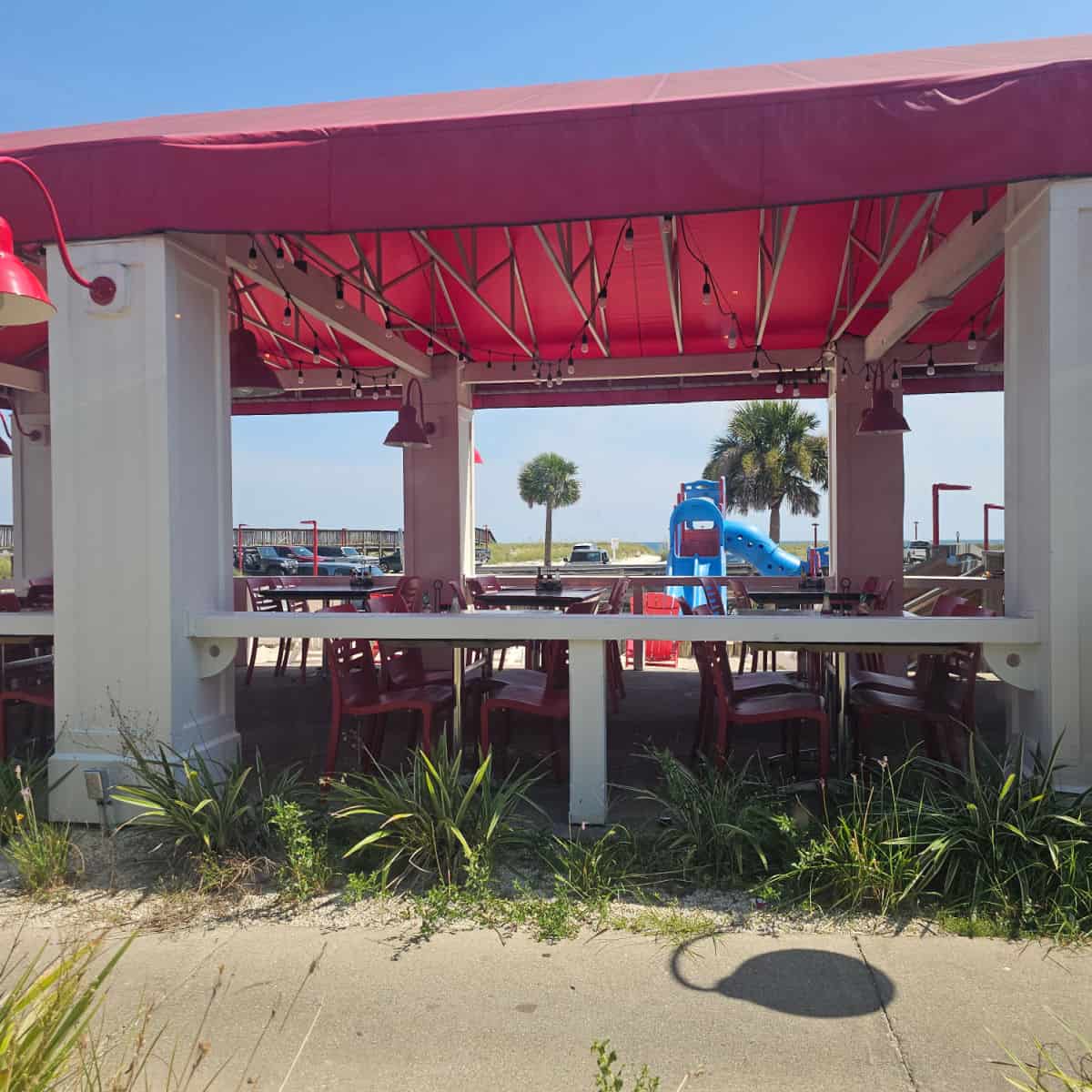 outdoor seating with tables and chairs under a red cover, kids play area in the background