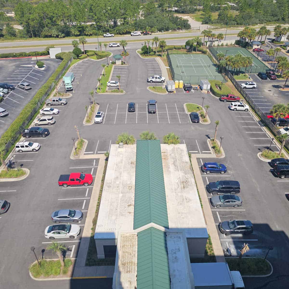 looking down over Shoalwater condo parking lot and indoor pool building with parking spread throughout the large lot, tennis court in the back corner and Perdido Beach Blvd in the background