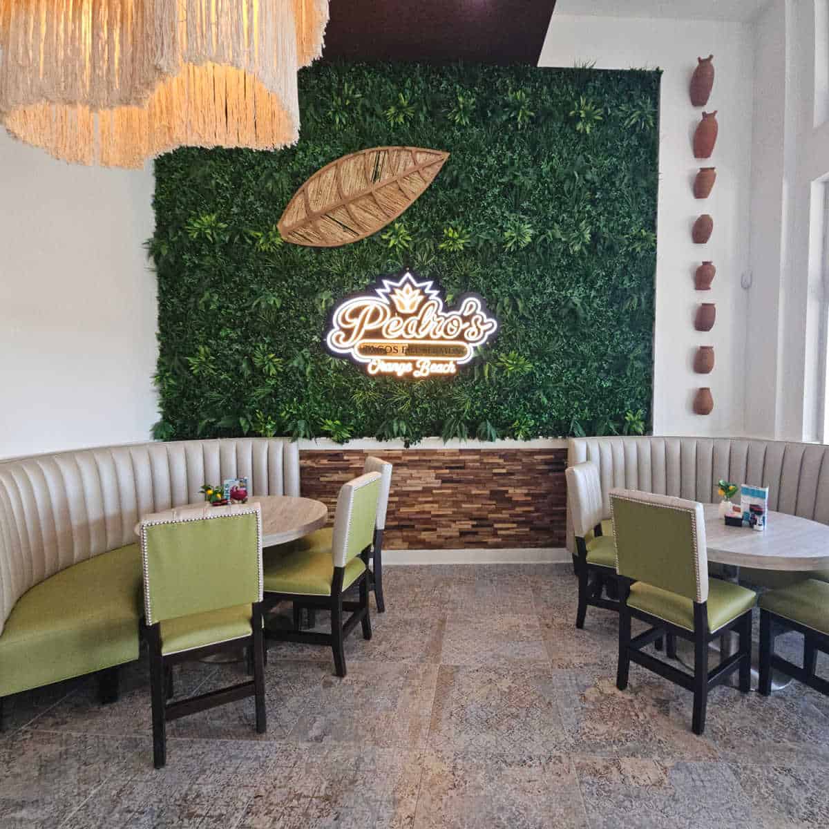Pedros sign on the back wall of greenery above two half booth tables with chairs