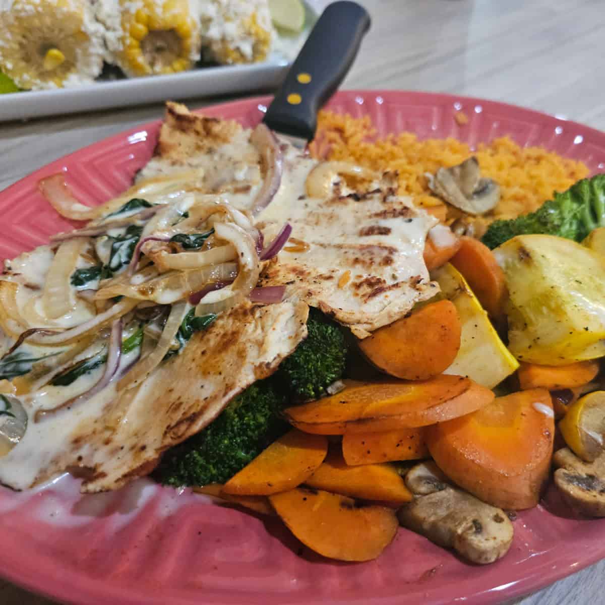 chicken covered in onions and sauce next to rice and veggies on a pink plate
