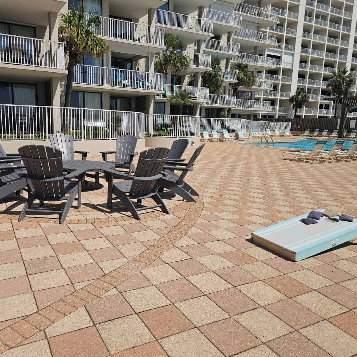 pool deck with Adirondack Chairs around a table, a cornhole game, and lounge chairs around the pool, shoalwater building in the background