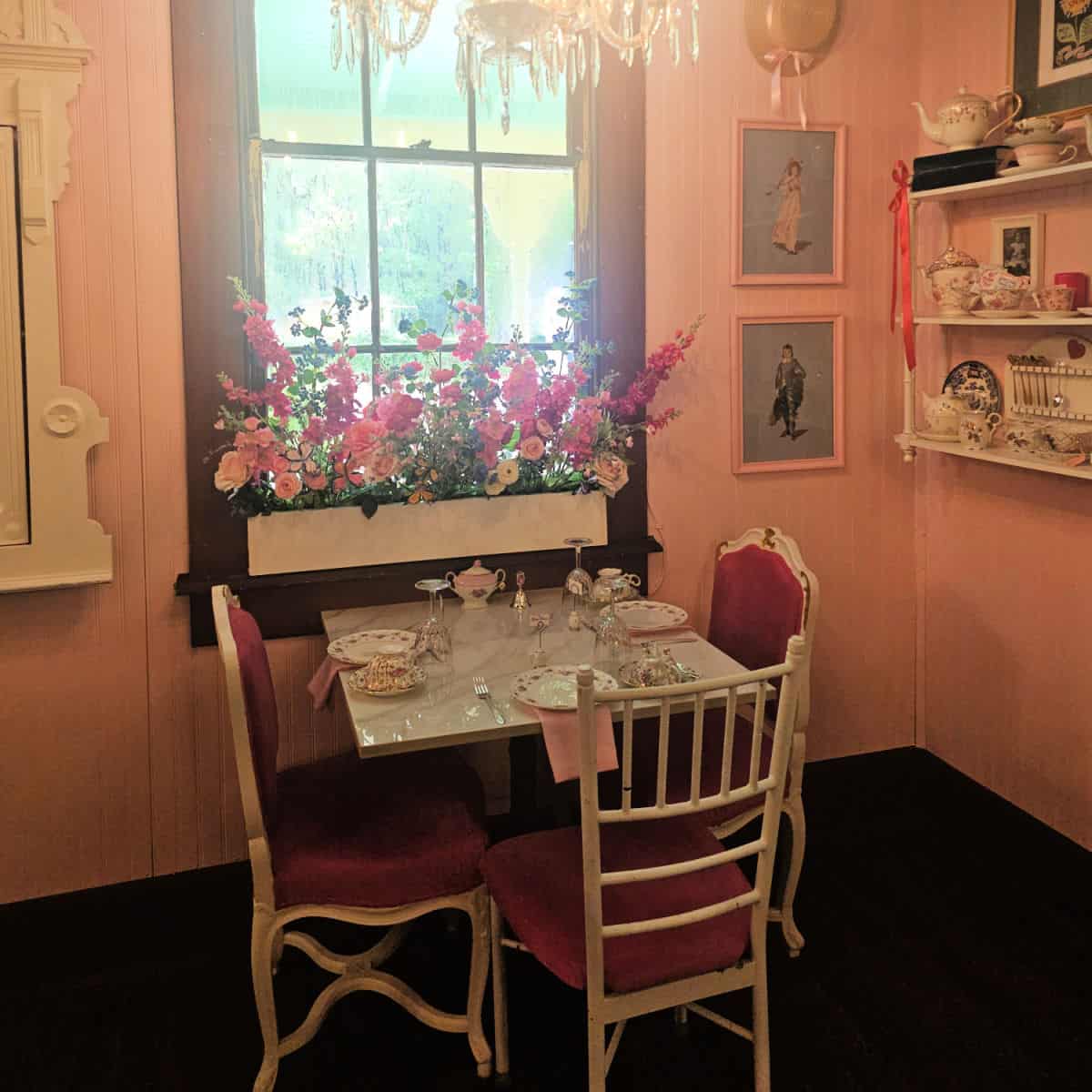 Charming Teacup interior with table with three padded pink seats, teacup and plates on the table, flower box in the window