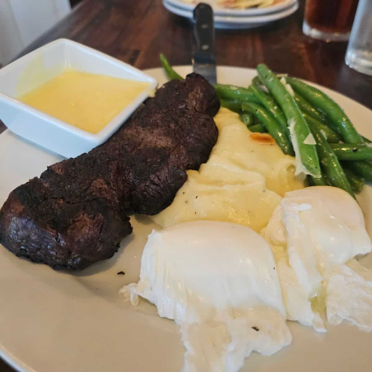 steak and eggs with green beans on a white plate