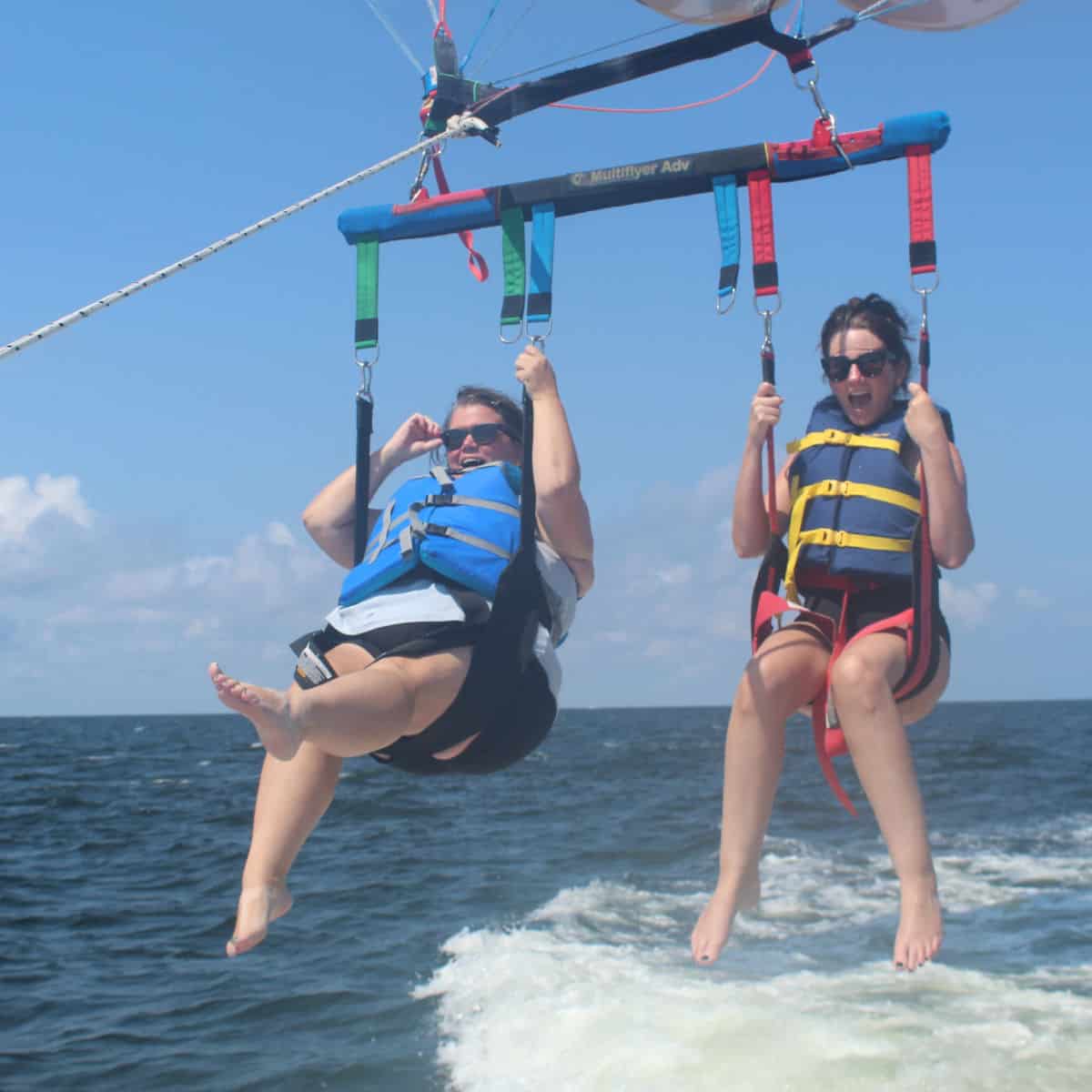 Tammilee and Amy parasailing with blue lifejackets and the Gulf below them.