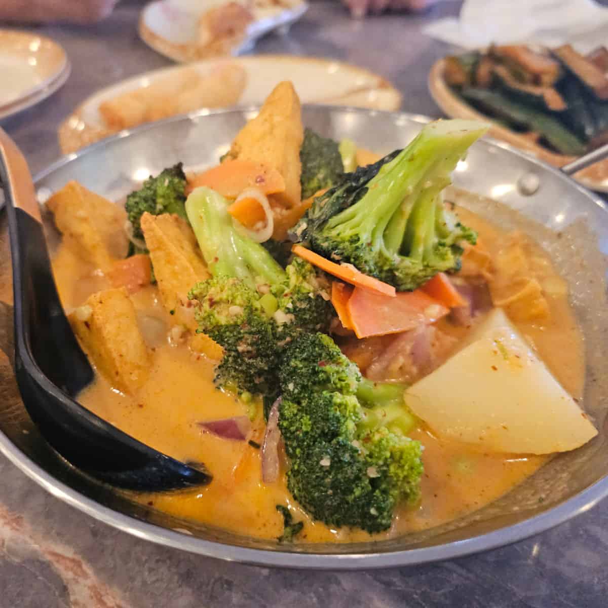 Curry with potatoes and vegetables in a silver bowl with a black spoon