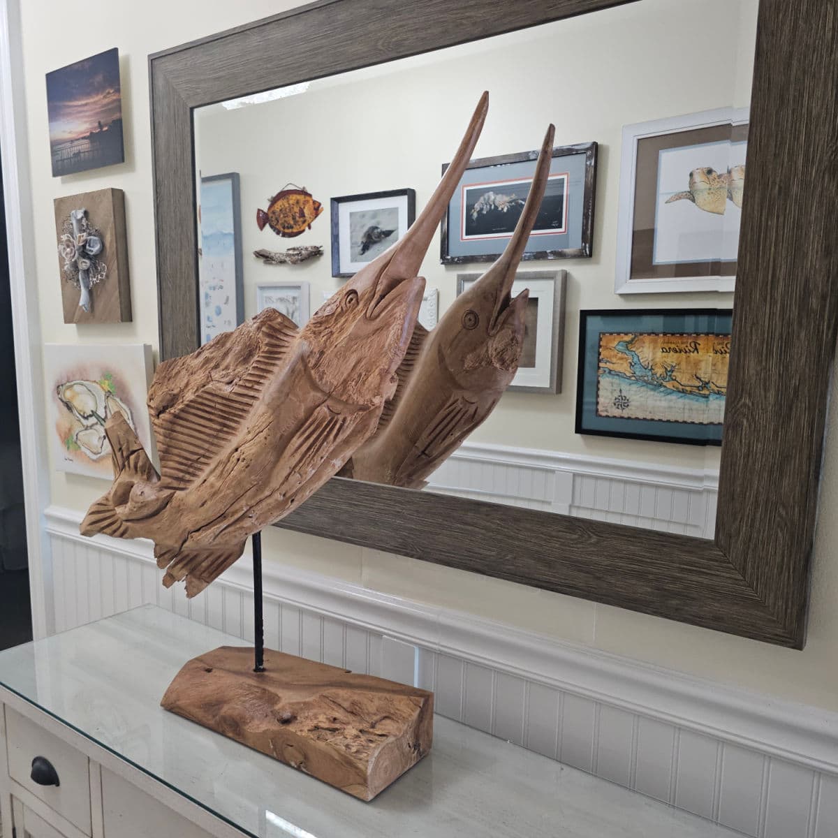 Wooden blue marlin sitting in front of a mirror reflecting art along the all